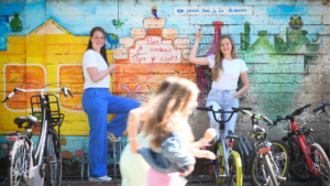 Tahnee en Stacey poseren voor een muurschildering waarop te lezen is: van pesten kom je in de nesten