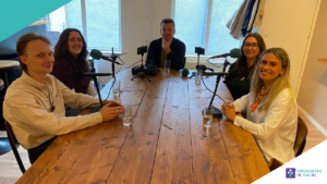 5 mensen aan tafel in podcastopstelling