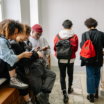 tieners in de gang op school, lopend met rugzak, zittend en kijkend op telefoon